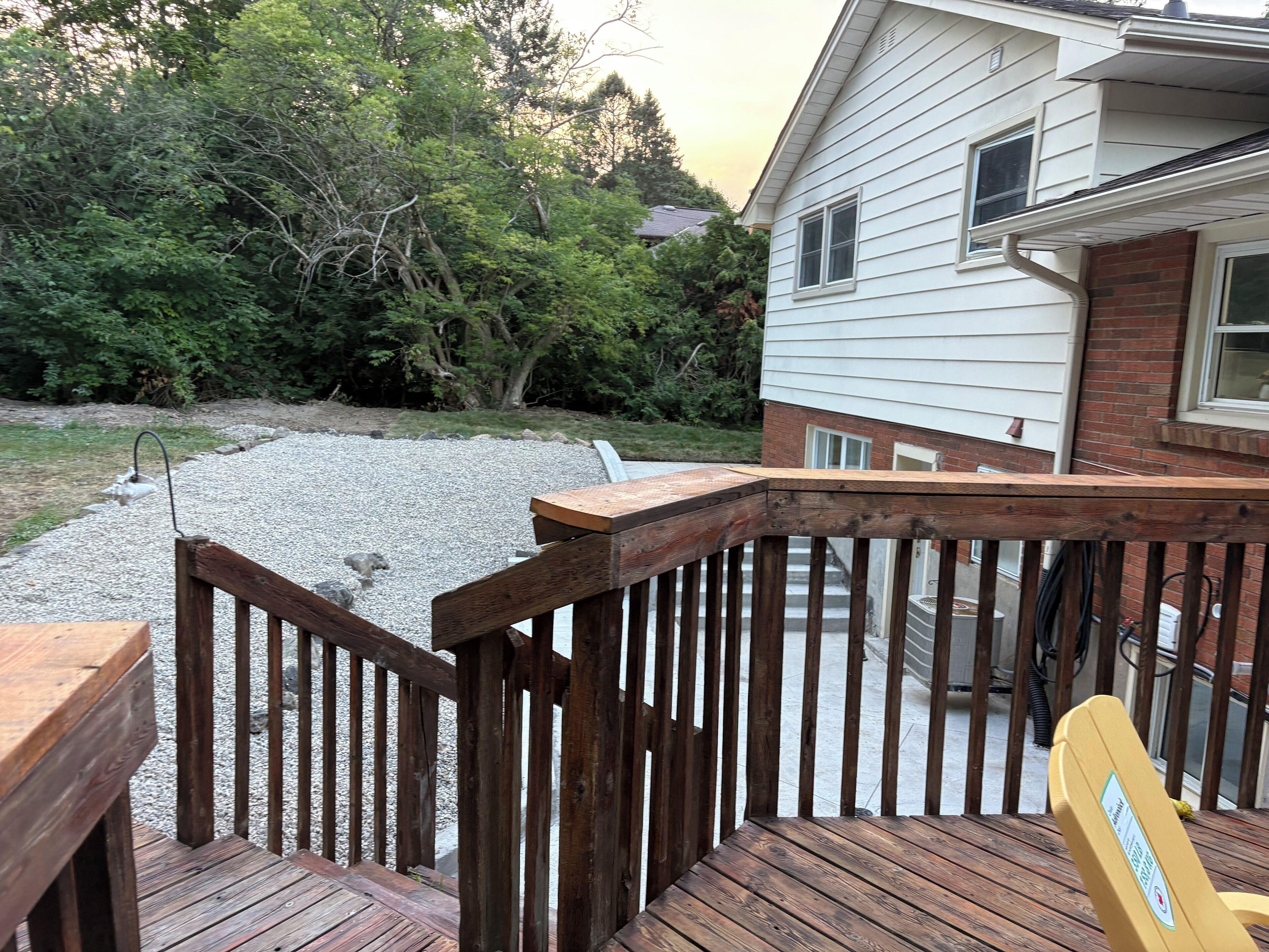 A wooden deck with a railing, a chair, and a house in the background.