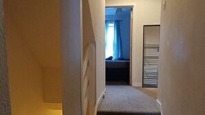 Un escalier menant à une chambre à coucher, où se trouvent un lit et une fenêtre avec des rideaux.