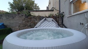 Un jacuzzi gonflable installé dans un jardin, avec un mur en pierre et une maison en arrière-plan.