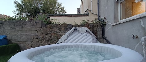 Una bañera de hidromasaje inflable en un patio trasero con un muro de piedra y una casa al fondo.