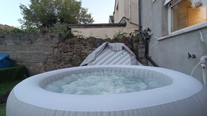 An inflatable hot tub in a backyard with a stone wall and a house in the background.