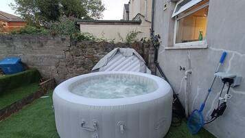 An inflatable hot tub in a backyard with a stone wall, a window, and a hose.