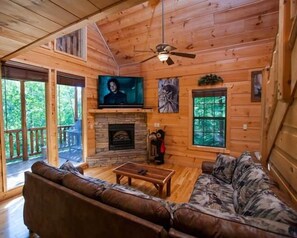 Ein Interieur einer Holzhütte mit Kamin, Fernseher und einer Couch.