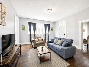 Ein Wohnzimmer mit Sofa, Sessel, Couchtisch und Fernseher.