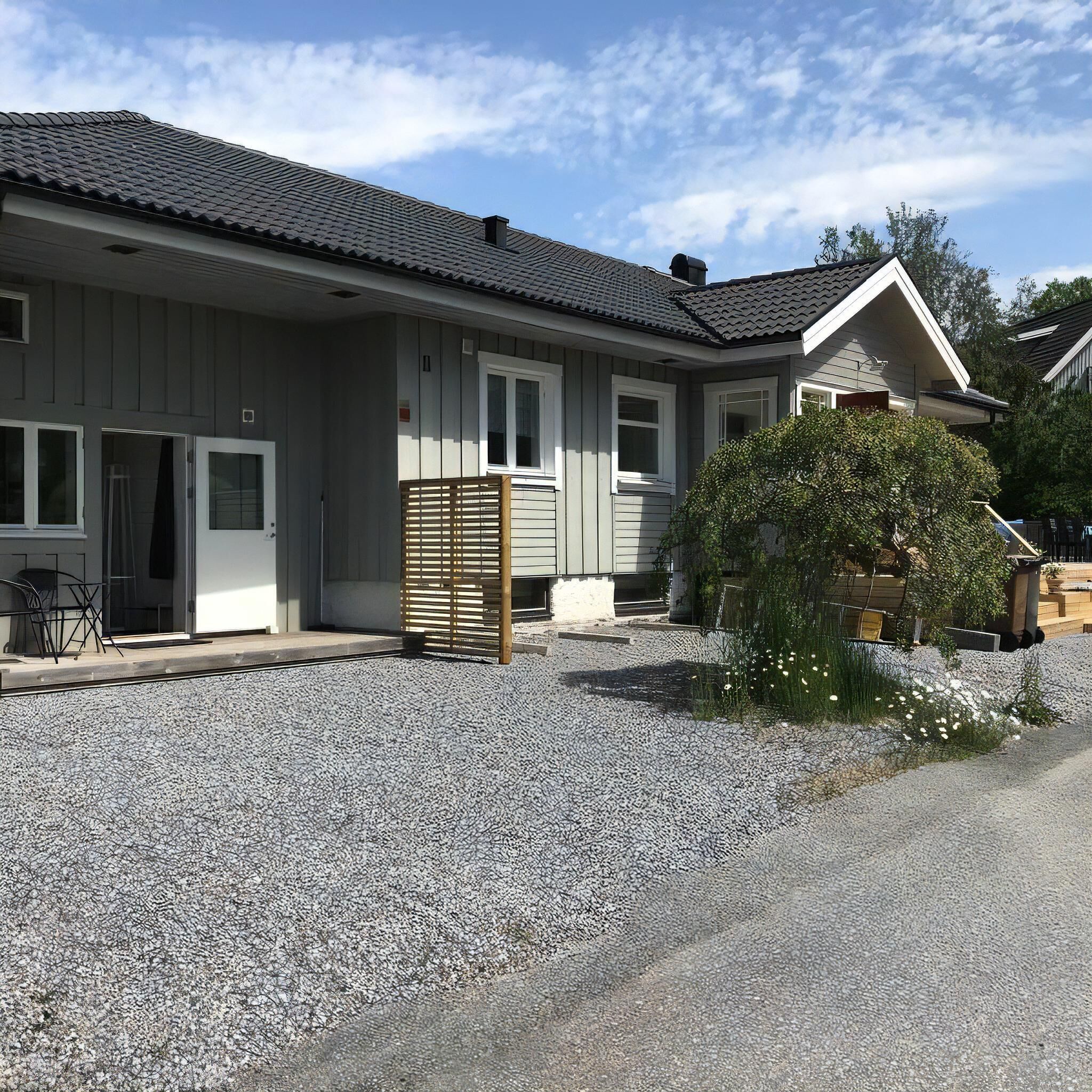 En bostadsbyggnad med en grusuppfart, ett trästaket och en liten trädgårdsyta.