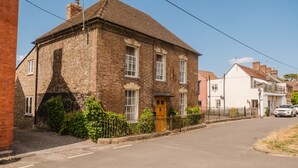 A two-story stone building with a traditional design, featuring a central entrance with a wooden door, multiple windows, and a small garden area with a fence. - Kempsey House -  Frampton on Severn, Gloucester, Tewkesbury (Frampton on Severn)