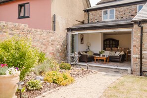 Een open terras met een zithoek, een bakstenen muur en een tuin met diverse planten.