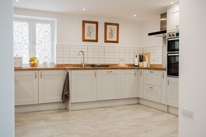 A modern kitchen with white cabinets, a stainless steel range hood, and a window with decorative curtains. - Kempsey House -  Frampton on Severn, Gloucester, Tewkesbury (Frampton on Severn)