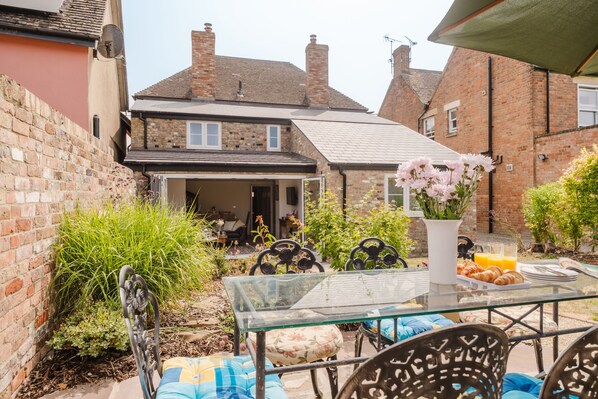 A glass table with chairs and a flower vase in a garden area.