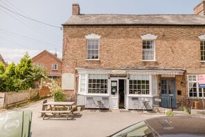 A traditional brick building with a cafe entrance, a wooden fence, and a car parked in front.