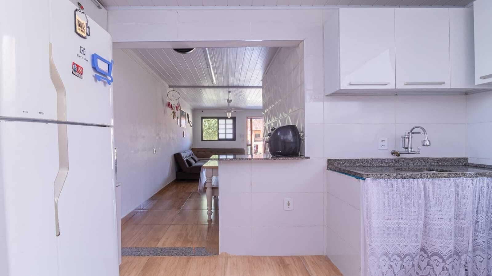 Une cuisine compacte avec des meubles blancs, un plancher en bois et une vue sur un espace de vie comprenant un canapé et une fenêtre.