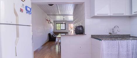 A compact kitchen with white cabinets, a wooden floor, and a view into a living area with a sofa and a window.