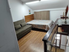 A bedroom with a bed, a sofa, a window with curtains, and a small table with a vase.