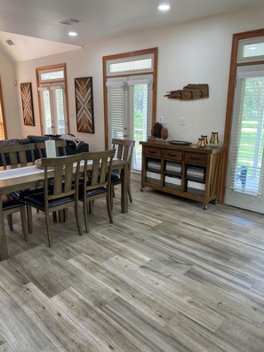 A dining area with a wooden table and chairs, a wooden cabinet with decorative items, and a view through the glass door.