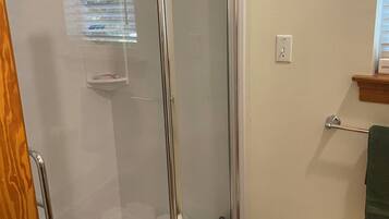 A glass-enclosed shower with a wooden door, a towel rack with a green towel, and a basket of white towels.