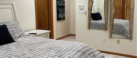 A bedroom with a bed, ceiling fan, wall-mounted artwork, and a mirror.