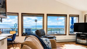 Una sala de estar con un ventanal grande, un televisor y vista al mar.