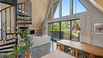 Un interior moderno estilo loft con una escalera en espiral, un comedor y grandes ventanales que ofrecen vistas al exterior.
