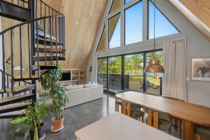 A modern loft-style interior with a spiral staircase, a dining area, and large windows offering a view of the outdoors.