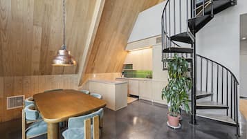 Eine moderne Küche mit Holzboden, ein Essbereich mit einem Holztisch und blauen Stühlen sowie eine schwarze Wendeltreppe.