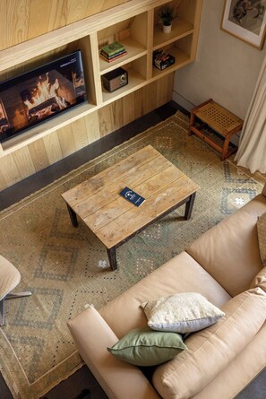 A living room with a television, a coffee table, a sofa, and a small wooden shelf.
