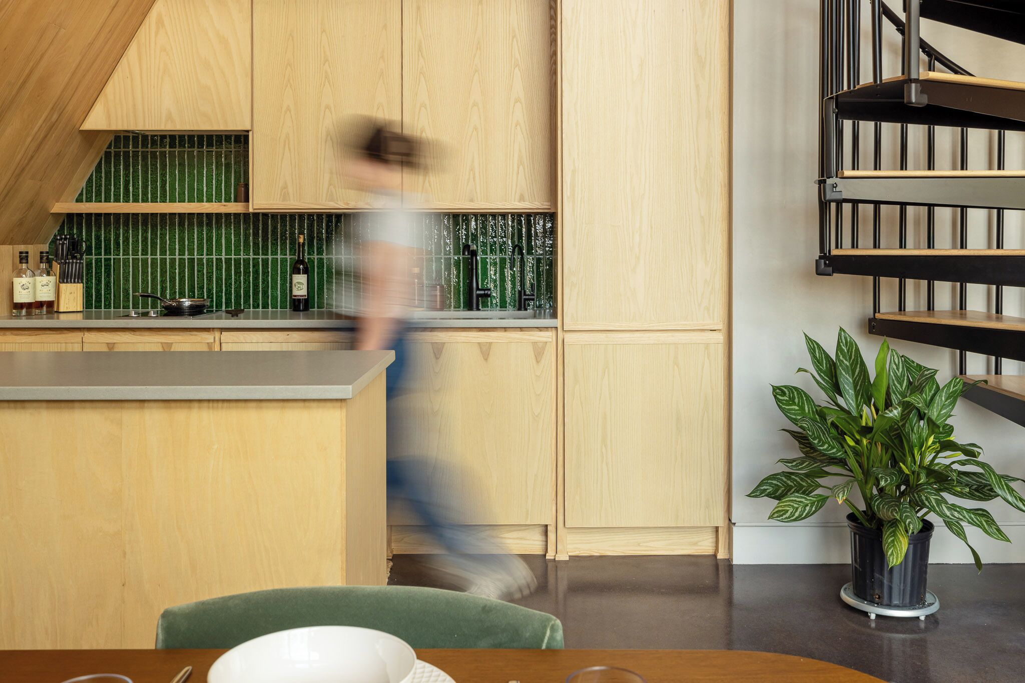 Una cocina moderna con armarios de madera, un salpicadero verde y una escalera negra.