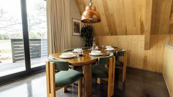 Un comedor con una mesa y sillas de madera, una lámpara colgante y vistas a través de un ventanal grande.