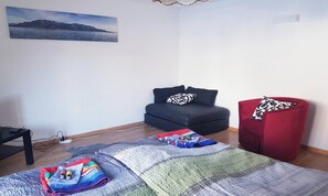 A room with a bed, a red chair, a black sofa, and a painting on the wall. - SPECTACULAR VIEWS OF THE MATTERHORN, THIS WELCOMING ZERMATT APARTMENT (Zermatt)