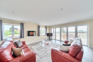 A spacious living room with a red leather sofa, a glass coffee table, and a flat-screen TV mounted on the wall. - The Donkey Shed -  Sherborne, Dorchester, sleeps 6 guests  in 3 bedrooms (Sherborne)