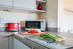 A kitchen with a red slow cooker, a microwave, a cutting board with tomatoes and green onions, and a wooden cutting board. - The Donkey Shed -  Sherborne, Dorchester, sleeps 6 guests  in 3 bedrooms (Sherborne)