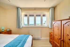 A bedroom with a bed, a wooden wardrobe, a radiator, and a window with curtains. - The Donkey Shed -  Sherborne, Dorchester, sleeps 6 guests  in 3 bedrooms (Sherborne)