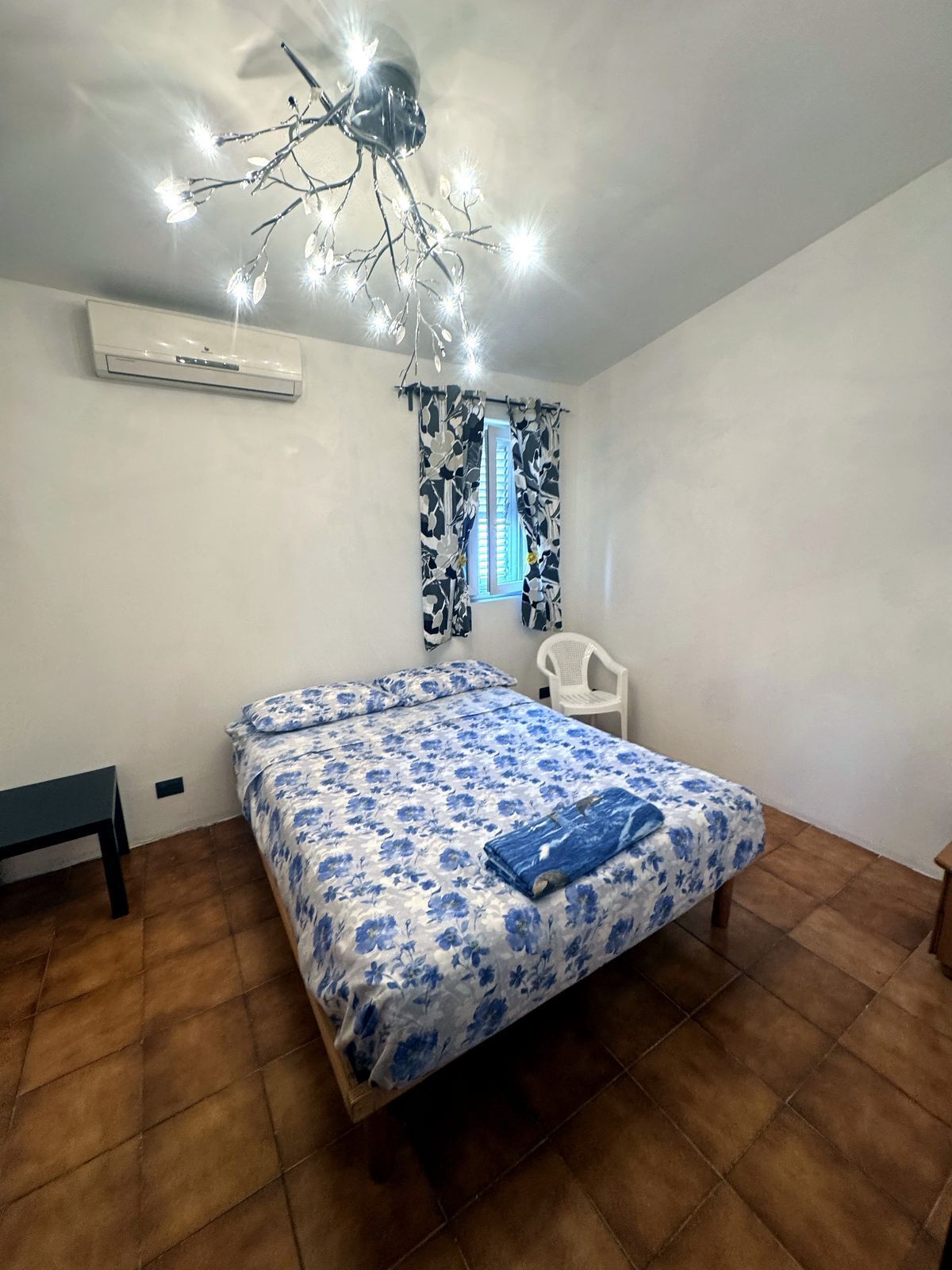 A bedroom with a bed, a chair, a ceiling light fixture, and a window with curtains.
