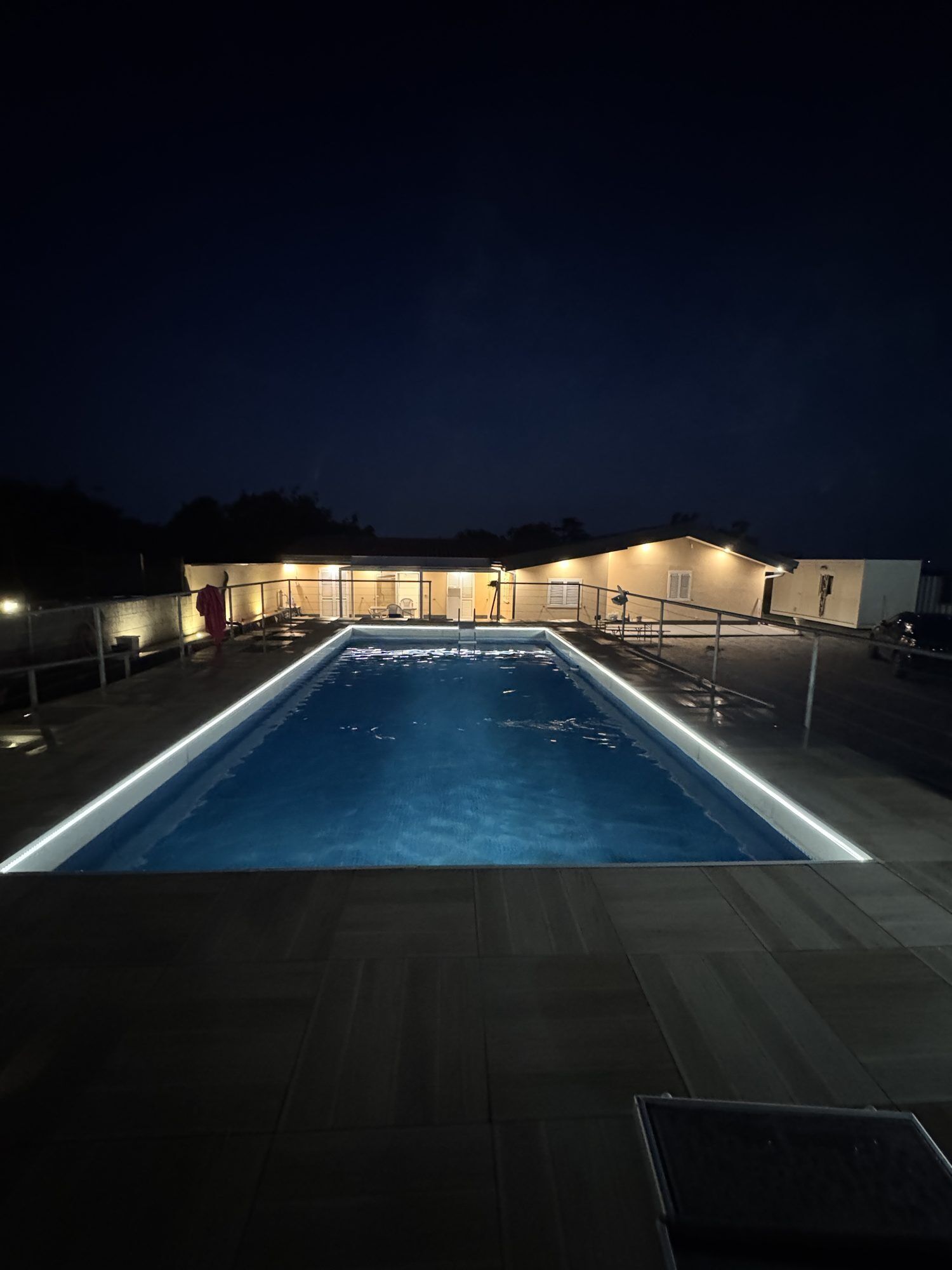 Piscina con plataforma de baldosas y zona cubierta con asientos.