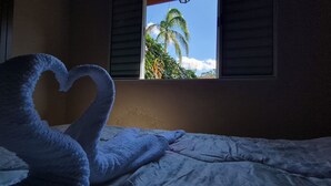 Ein Bett mit einem herzförmigen Kopfkissen und einem Fenster mit Blick auf Palmen.