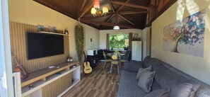 Una sala de estar con televisor de pantalla plana, una guitarra, un sofá y un comedor con sillas y una mesa.