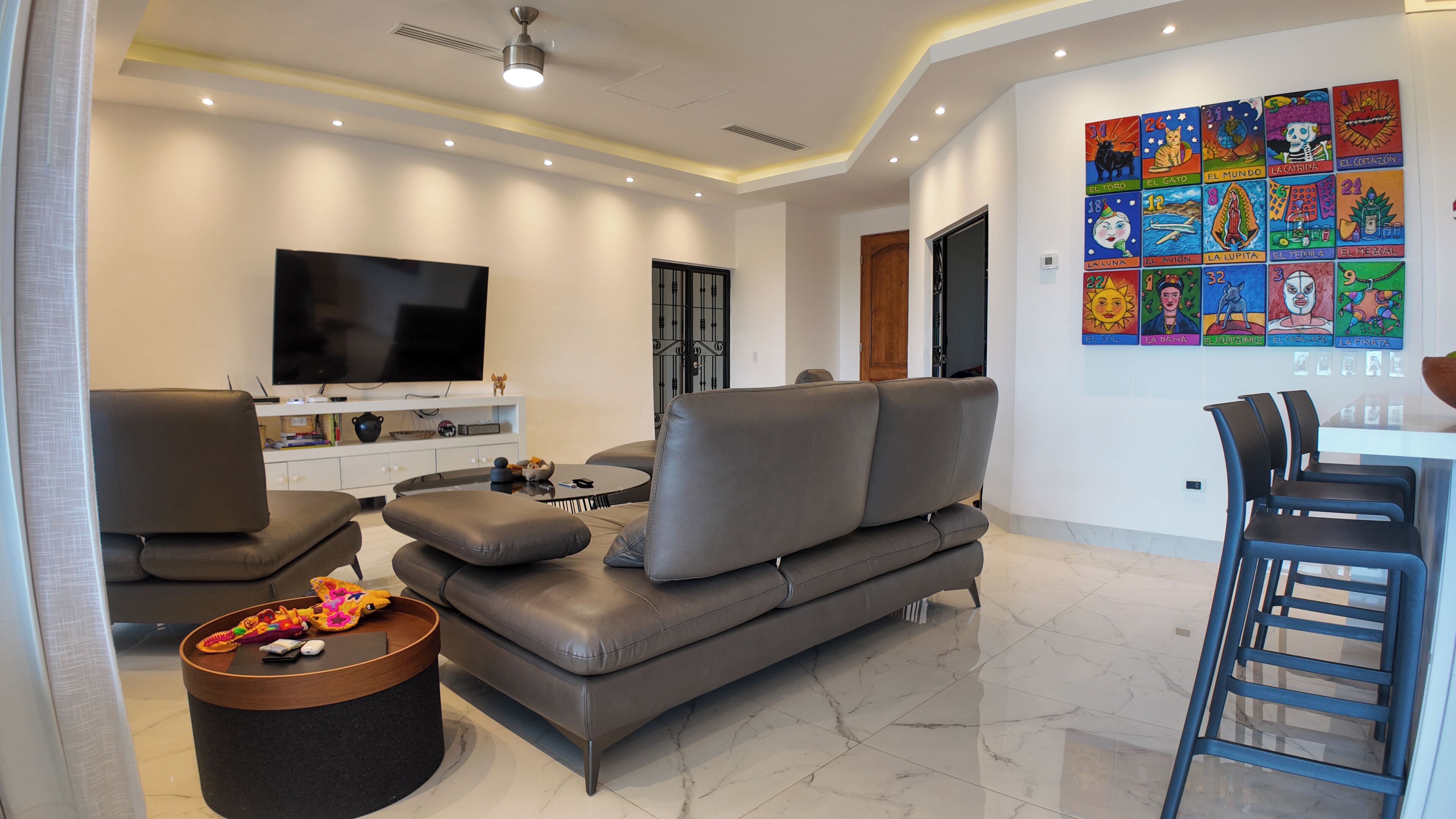 A modern living room with a grey sofa, a flat-screen TV, a coffee table, and a dining area with chairs.