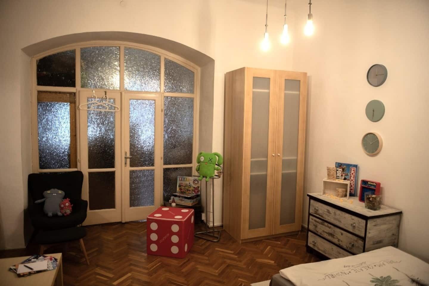 A room with a large arched window, a wardrobe, a desk with a chair, and a bed.