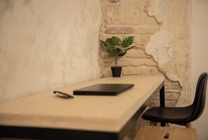 Ein schlichter Arbeitsplatz mit einem Holztisch, einem schwarzen Stuhl, einem Tablet und einer Topfpflanze.