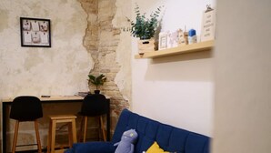A room with a blue sofa, a small table, two chairs, a wall with a brick pattern, and a shelf with various items. - Spacious 2bedroom apartment, 4 beds in the DOWNTOWN with FREE PARKING and AC (Budapest)