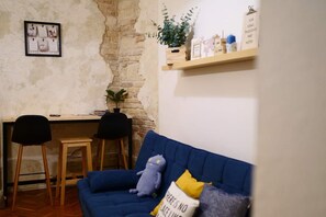 Ein Zimmer mit einem blauen Sofa, einem kleinen Tisch, zwei Stühlen, einer Ziegelwand und einem Regal mit verschiedenen Gegenständen.
