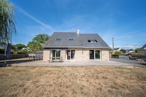 Uma casa de dois andares com fachada de pedra, um alpendre coberto com uma mesa de piquenique e um céu azul límpido.