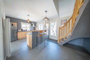 A modern kitchen with a central island, bar stools, and a staircase with wooden railings. - Havre de Paix Familial à Deux Pas des Plages (Erdeven)