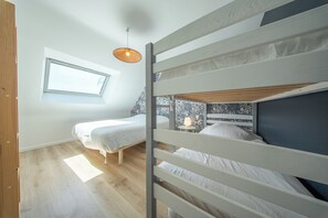 Ein kleines Schlafzimmer mit Etagenbett, einem Einzelbett, einem Dachfenster und einer Pendelleuchte.