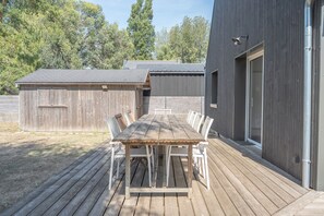 Um deck de madeira com mesa e cadeiras, um depósito e um edifício com uma grande janela.