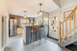 A modern kitchen with a central island, stainless steel appliances, and a wooden staircase. - Havre de Paix Familial à Deux Pas des Plages (Erdeven)