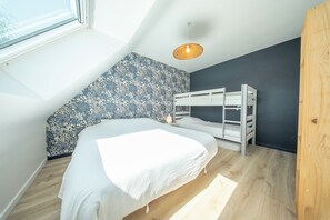 Quarto com cama beliche, uma cama de solteiro, parede estampada, luminária pendente e uma janela.
