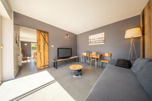 Ein modernes Wohnzimmer mit Flachbildfernseher, einer Couch, einem Couchtisch und einem Essbereich mit Stühlen und Tisch.