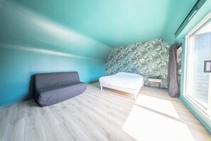 A room with a grey sofa, a white bed, and a wall with a leafy pattern. - Havre de Paix Familial à Deux Pas des Plages (Erdeven)