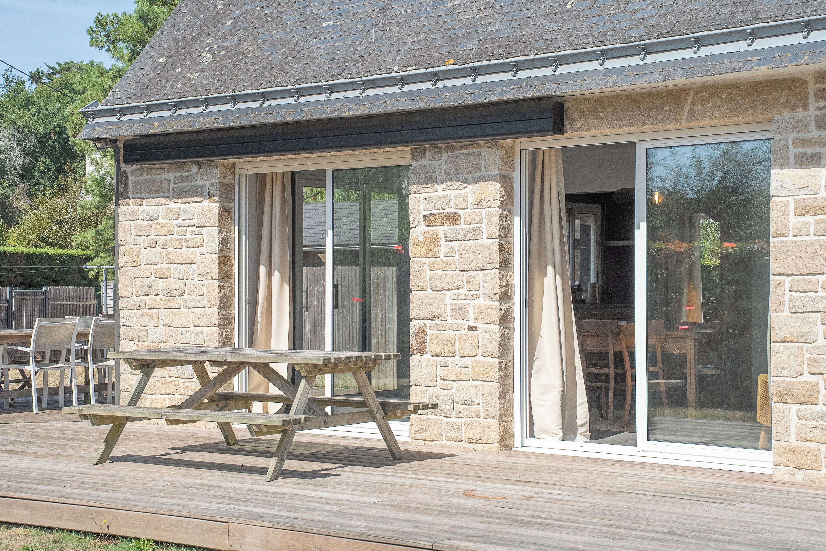 Un bâtiment en pierre doté d’une terrasse en bois, d’un espace extérieur aménagé pour s’asseoir et d’une grande porte-fenêtre coulissante.