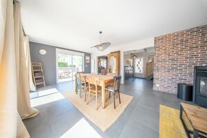 Ampla sala de estar com mesa de jantar, cadeiras, lareira e vista para o exterior.